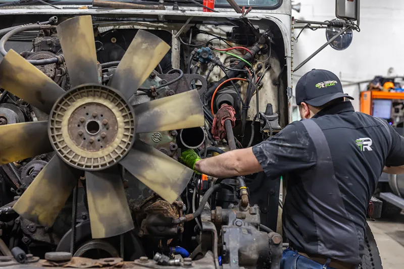 Technician performs heavy-duty engine repair on an exposed truck engine.