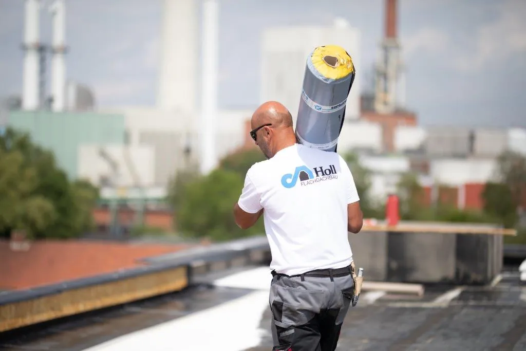 Ein Dachdecker trägt Material über ein Flachdach