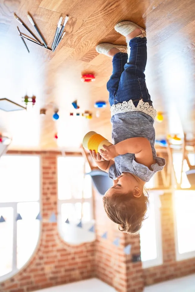 A child playing in a bright room with brick walls, big arched windows, and a wooden floor