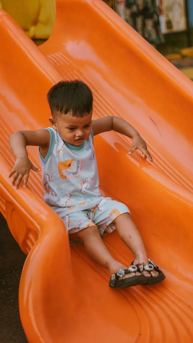 A child going down an orange plastic slide on a playground