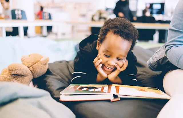 A child smiling as he reads a book on the couch