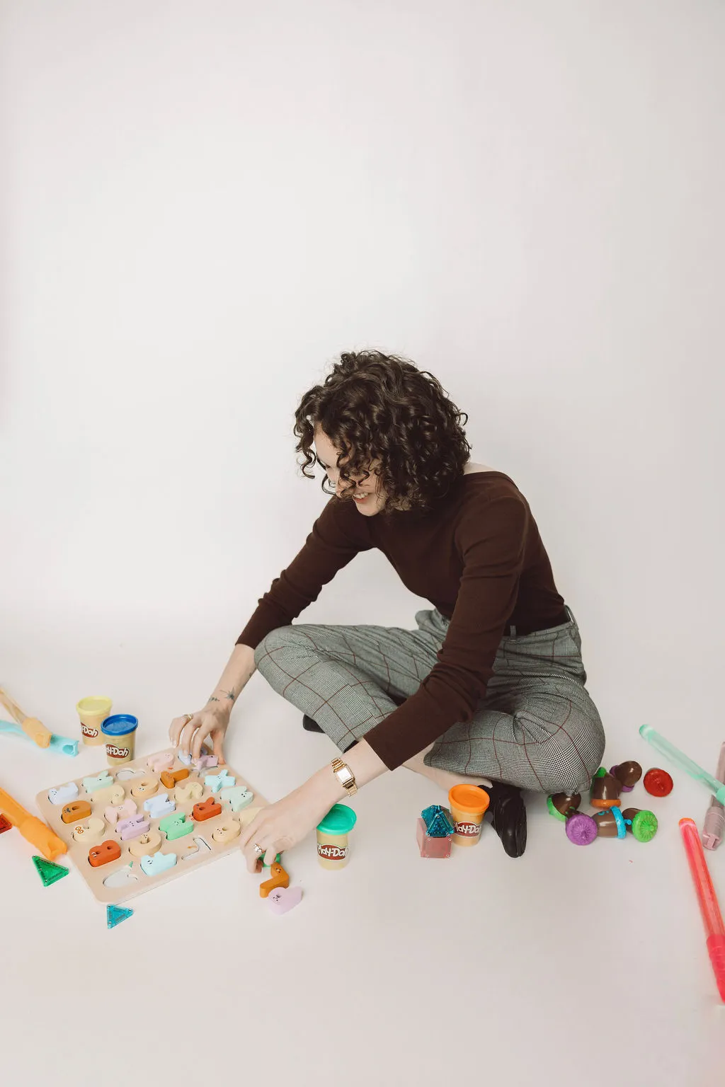 Tori sitting on the floor playing with some children's toys – a wooden alphabet board, play-dough, colored acorns, etc.