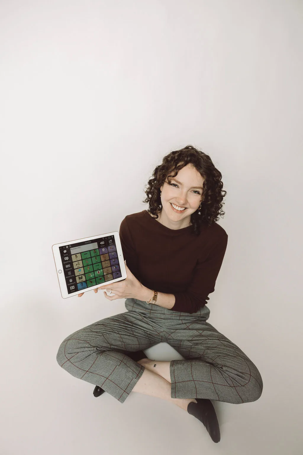 Tori smiling and sitting on the floor showcasing an iPad with a speech-language app