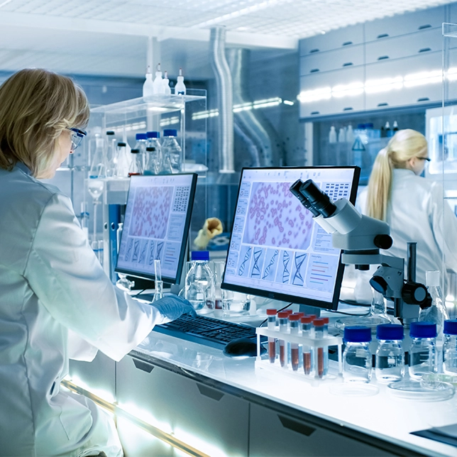 Researcher in a lab using computers and a microscope to analyze biological samples
