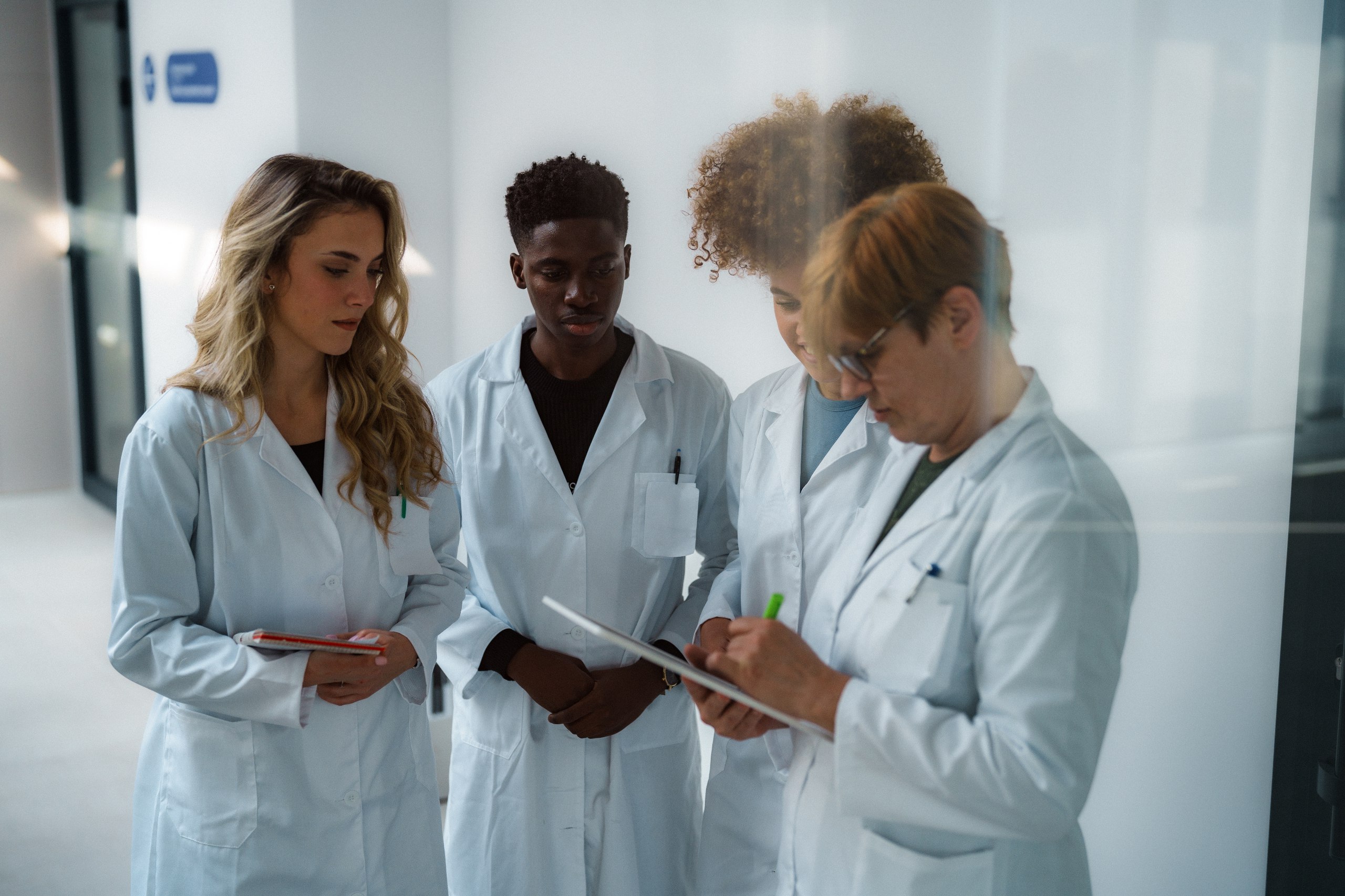 Four healthcare workers in lab coats discussing medical notes and research in a bright environment