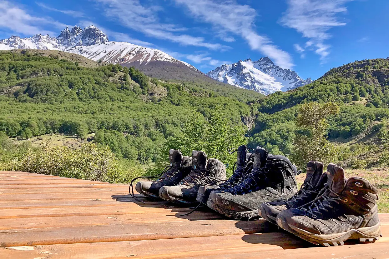Hiking boots resting on a deck with Cerro Castillo’s snow-covered peaks in Patagonia