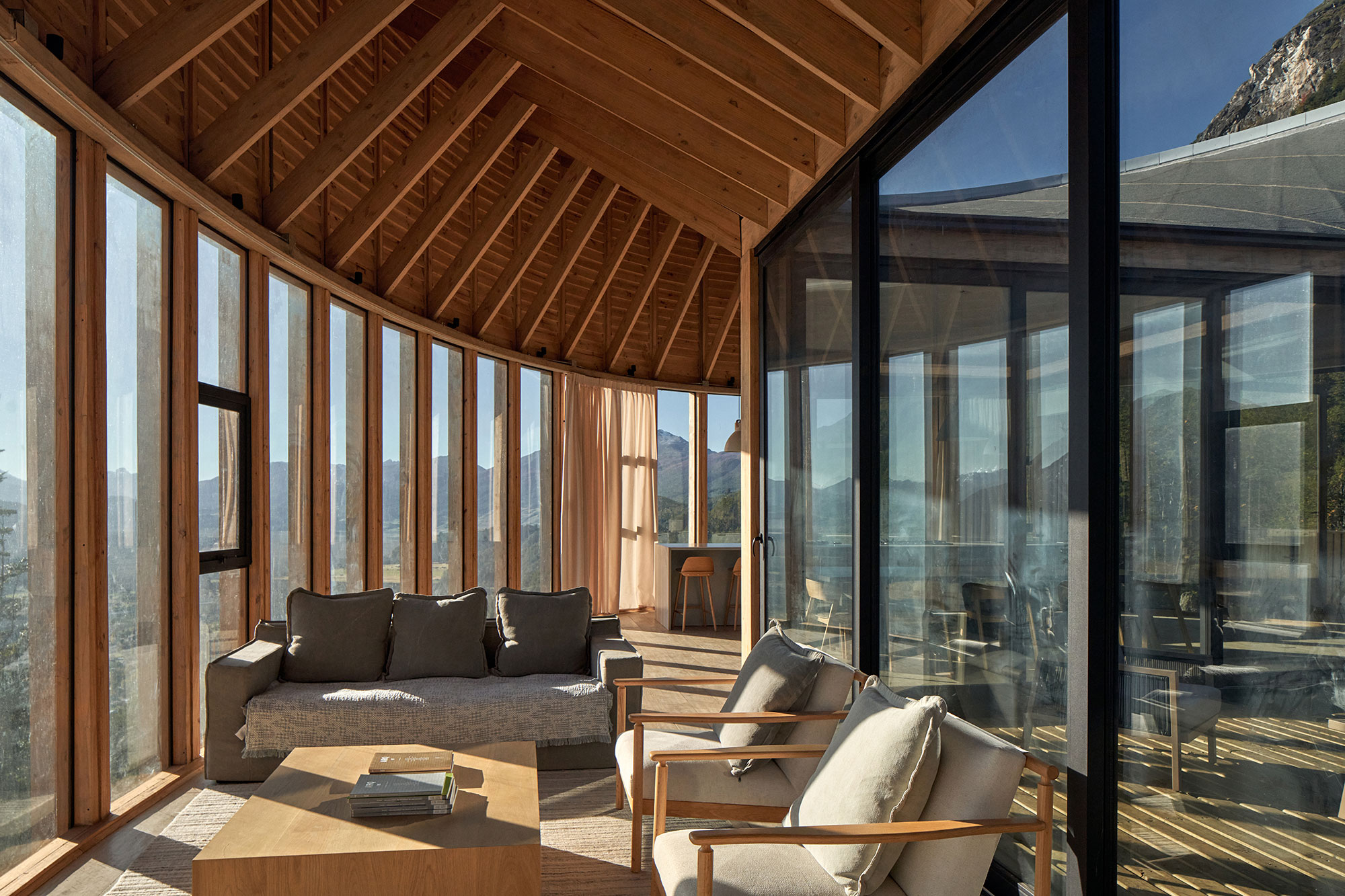 Lounge area with warm Lenga wood interiors and Patagonian mountain views through glass walls