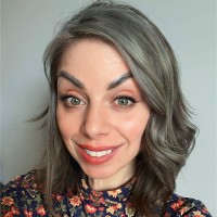 Melissa Randazzo smiling with shoulder-length wavy gray-brown hair, wearing a floral high-neck top, in front of a neutral background.