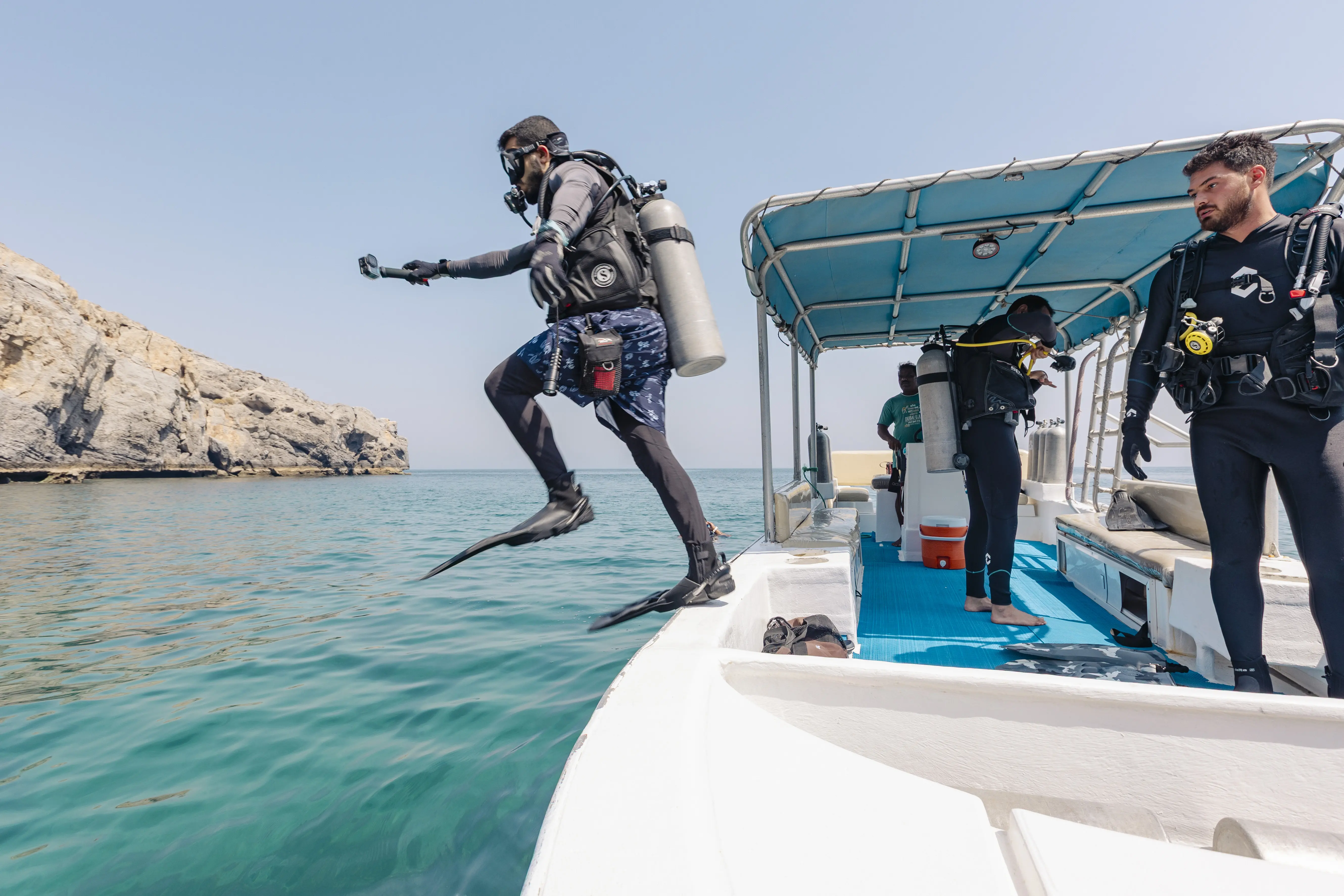 A scuba diver performs a giant stride entry into the water from the side of a dive boat.

