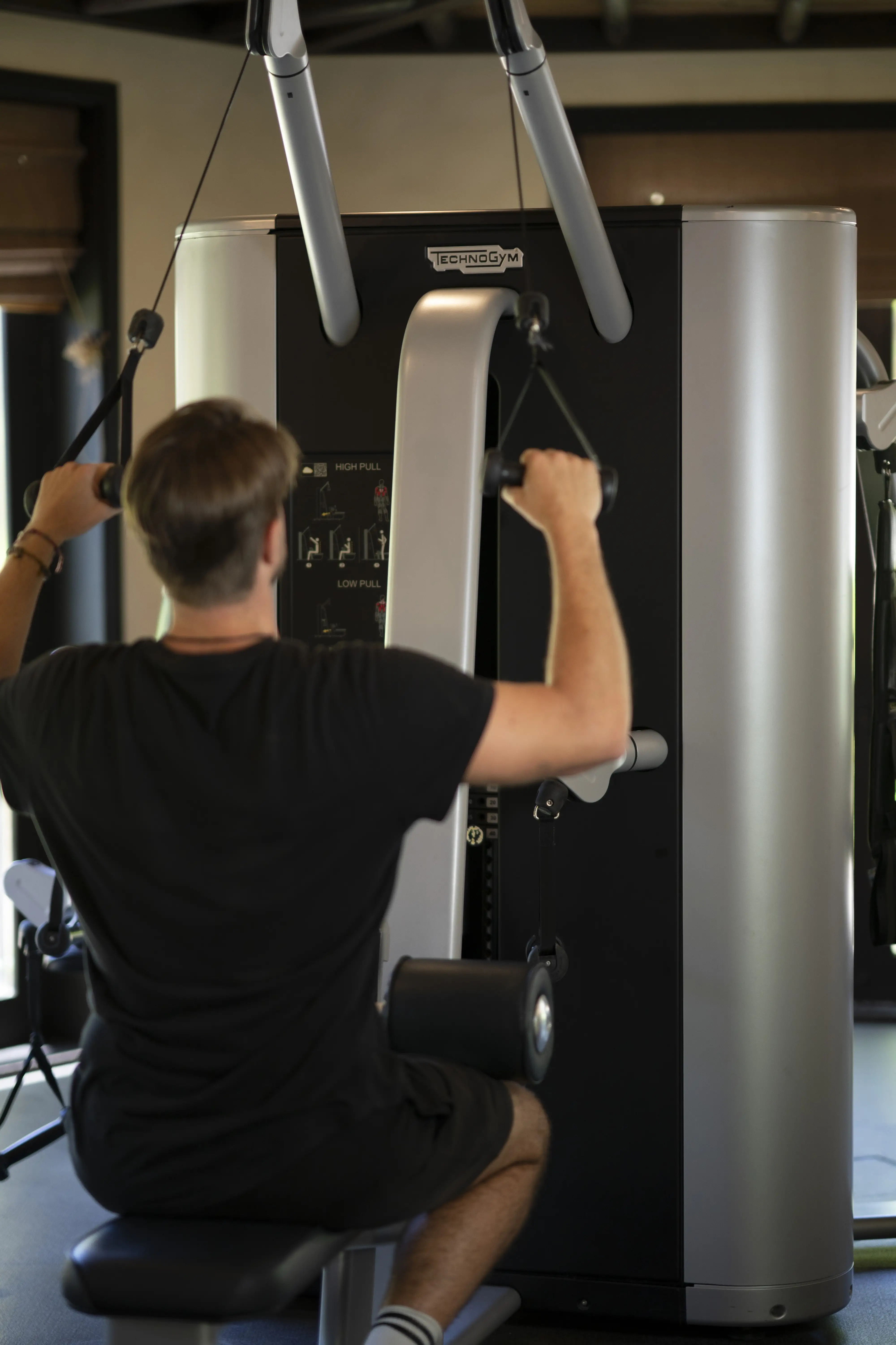 A man performs a lat pulldown exercise on a modern Technogym machine in the fitness center.


