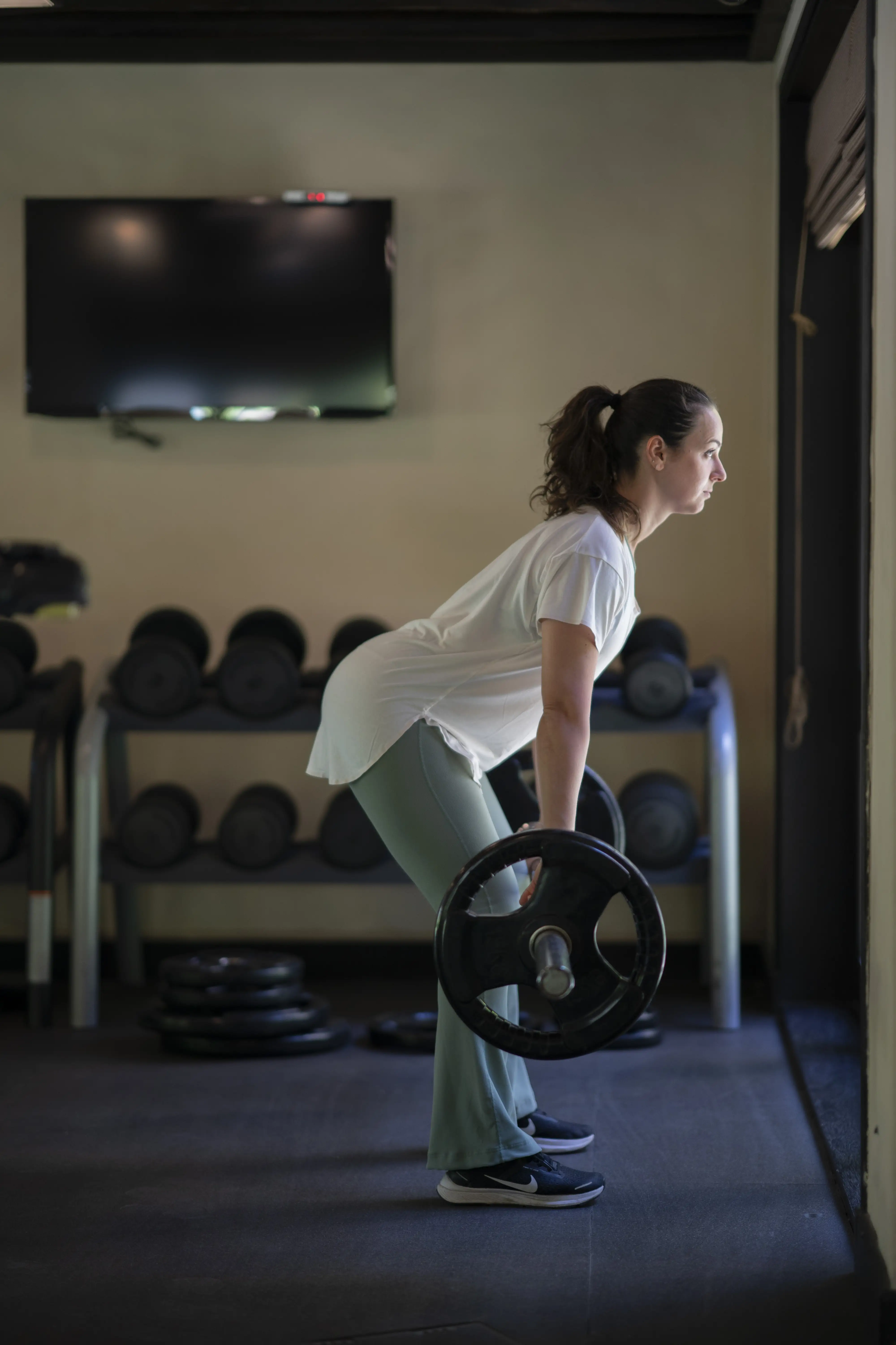 A woman performs a deadlift with a barbell in the free weights section of the hotel gym.