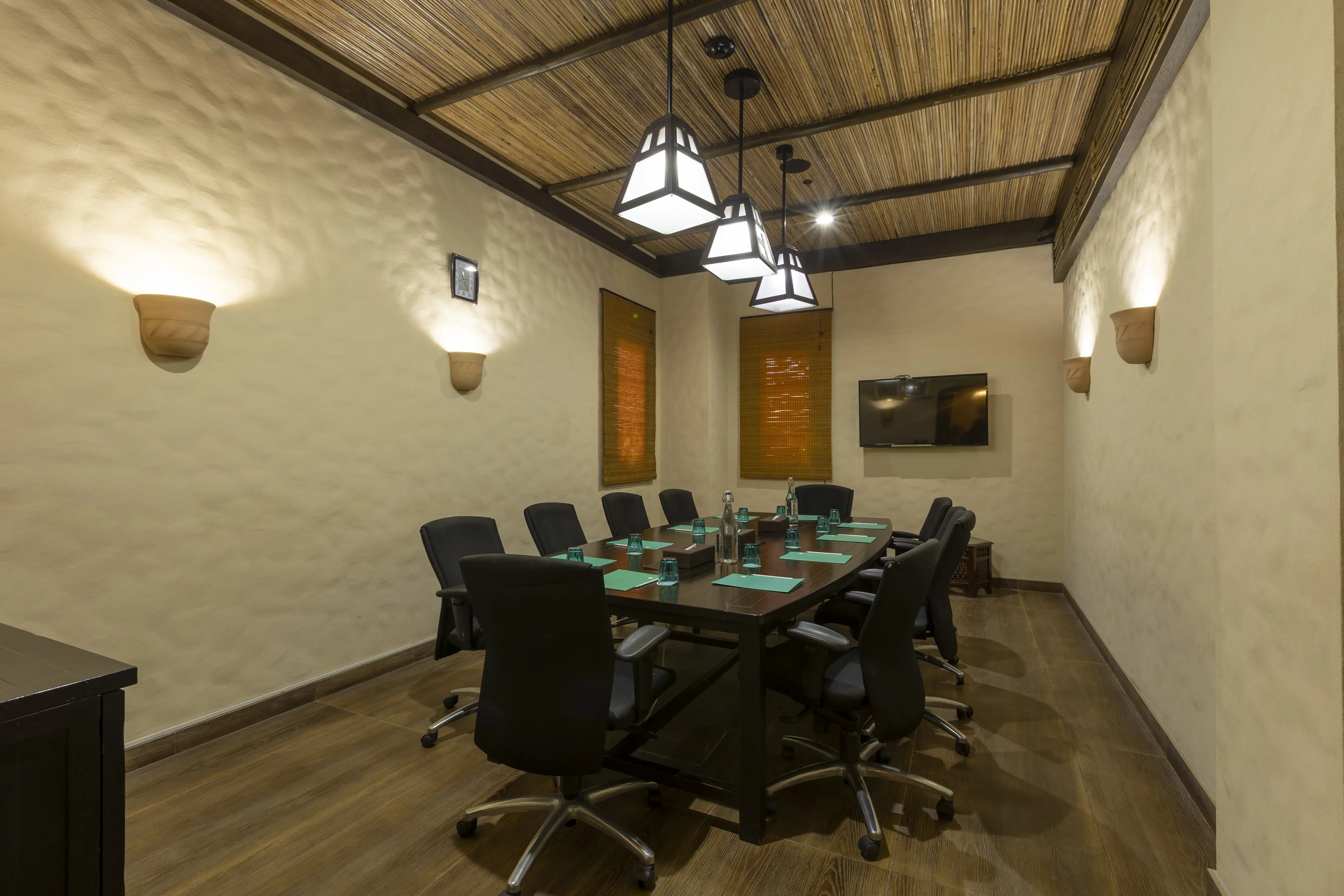 A room with a long desk, surrounded by chairs on wheels. 3 Arabic style lantern lamps hang from the cieling.