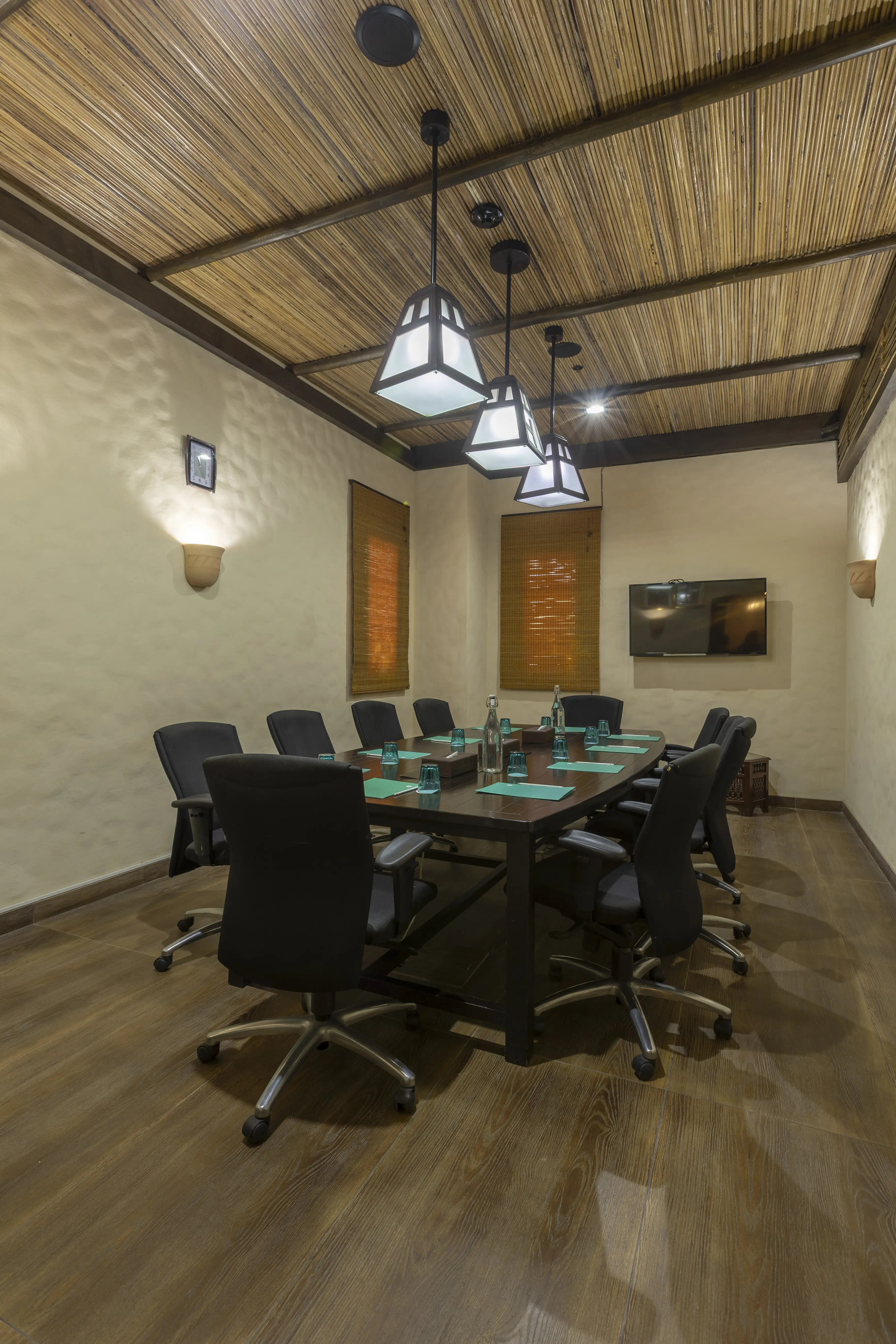 A room with a long desk, surrounded by chairs on wheels. 3 Arabic style lantern lamps hang from the cieling.