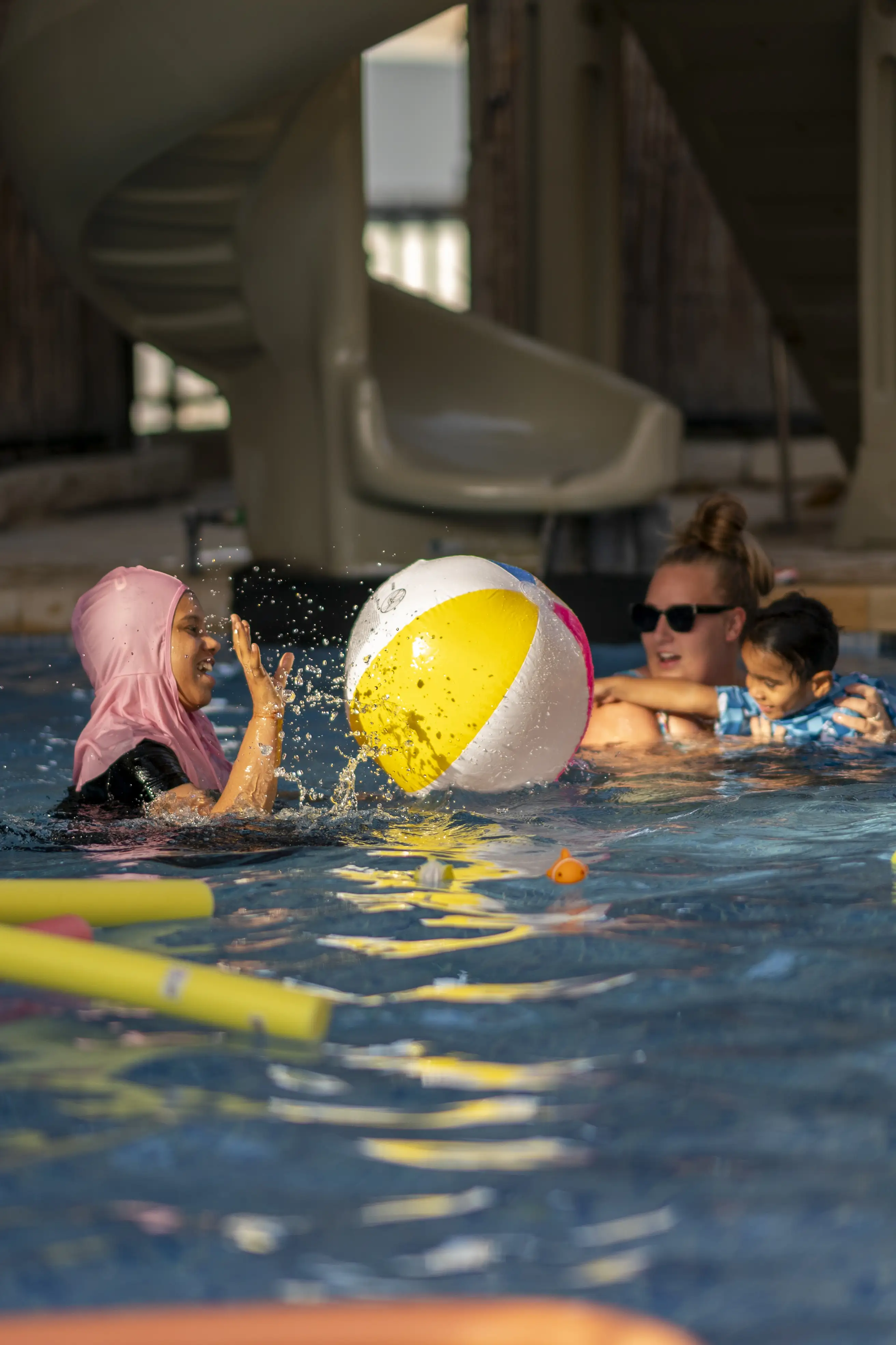 Children and an adult play together with a colorful beach ball in the kids' swimming pool.

