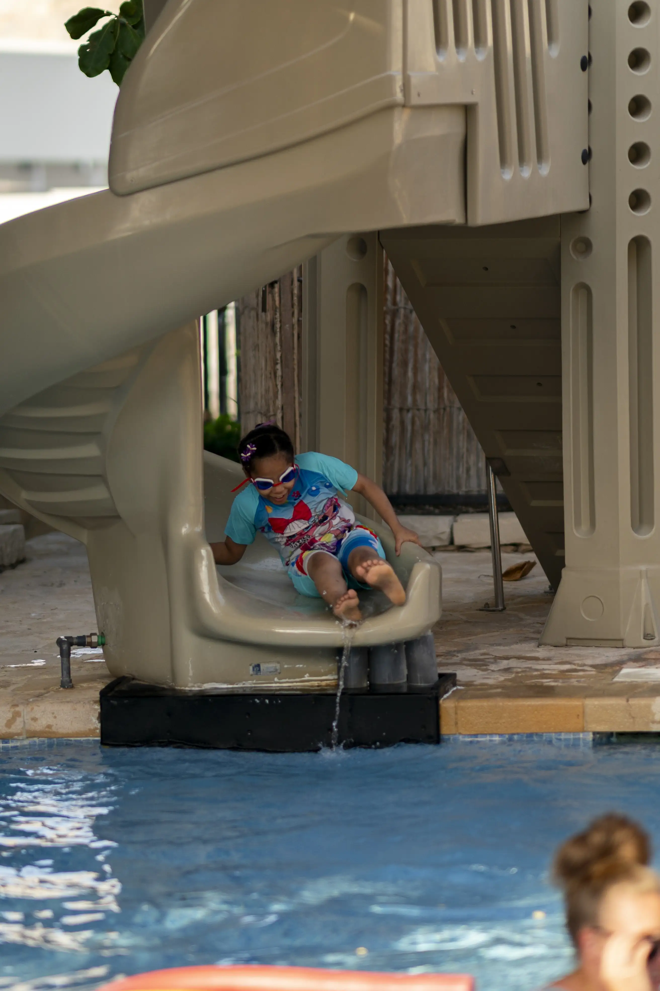A young girl laughs as she splashes into the water at the bottom of the kids' pool slide.