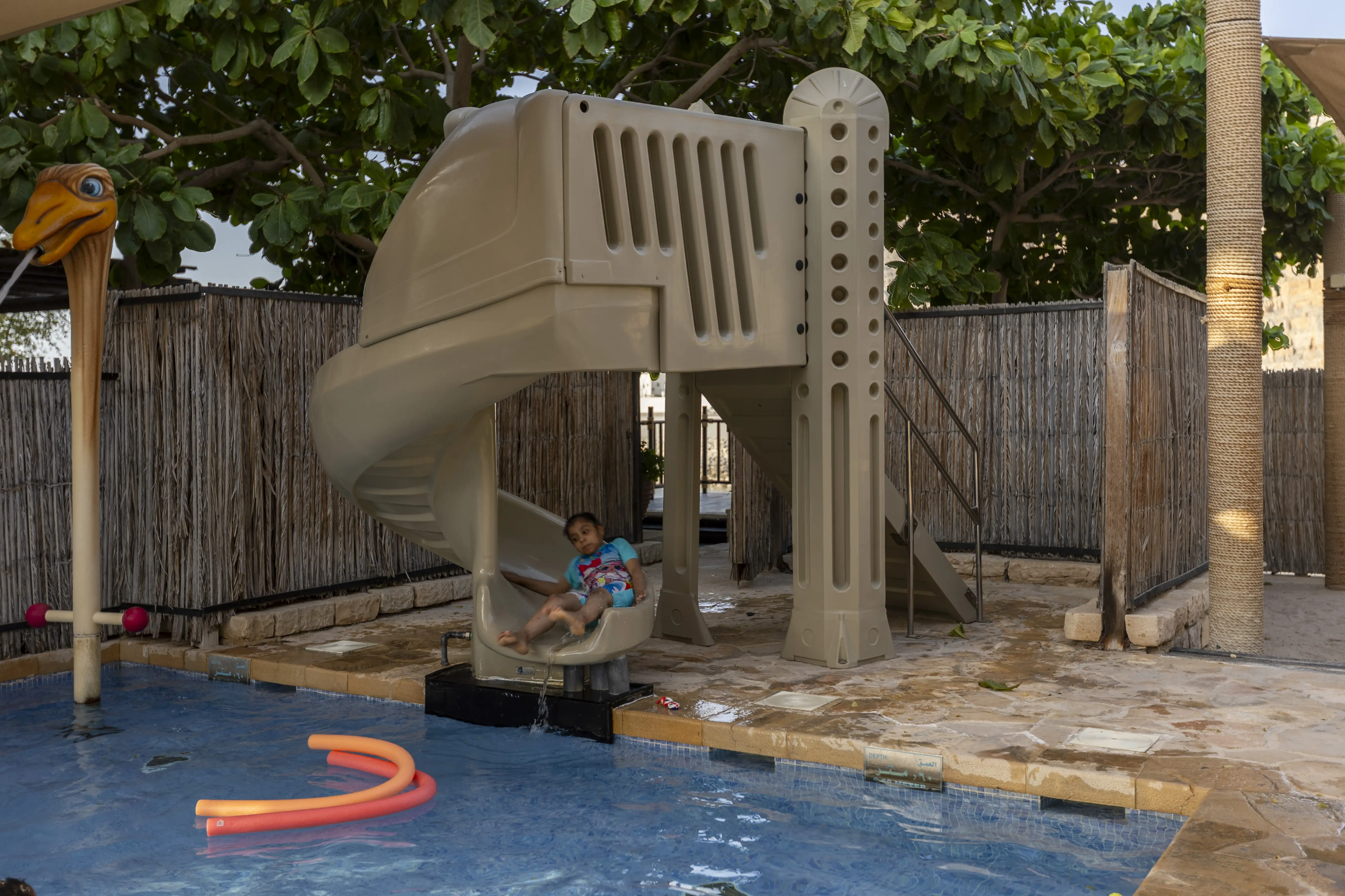 The kids' club pool area at Atana Musandam, featuring a water slide, a fun shower, and a safe, shaded environment for children.