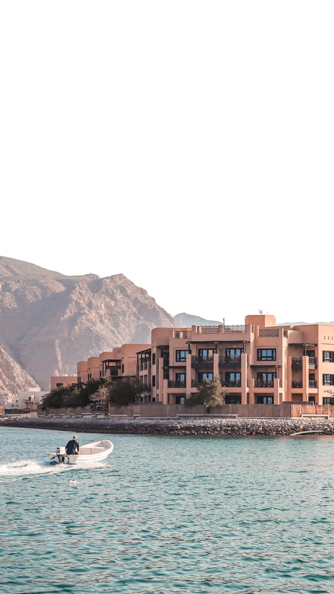Part of a parallax effect. This foreground layer moves at a different speed to the background layer, creating a parallax effect. Atana Musandam property image taken from the water with the mountains in the background. A small speedboat rides in from the left of the image.