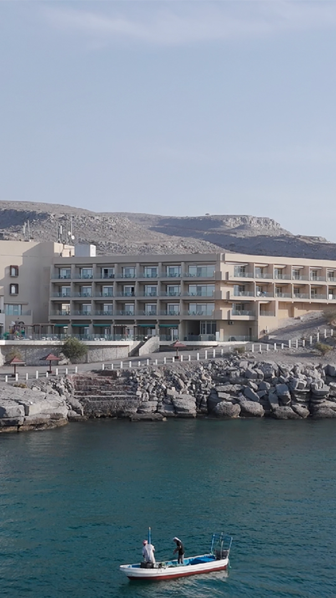 Atana Khasab hotel from the sea, with 2 fishermen on a small boat in front.