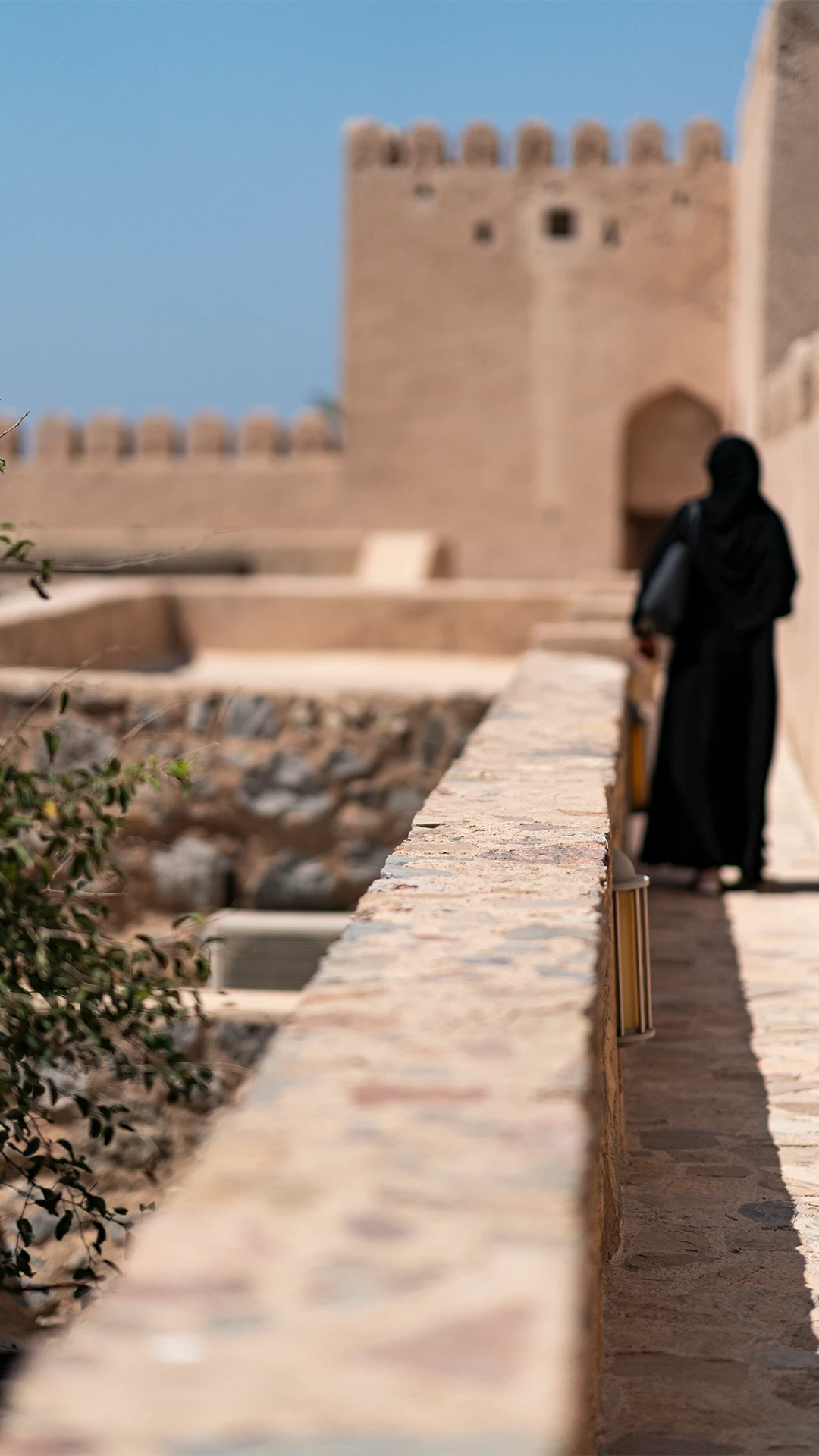A guest walks along the stone ramparts of the historic Khasab Fort on a sunny day.