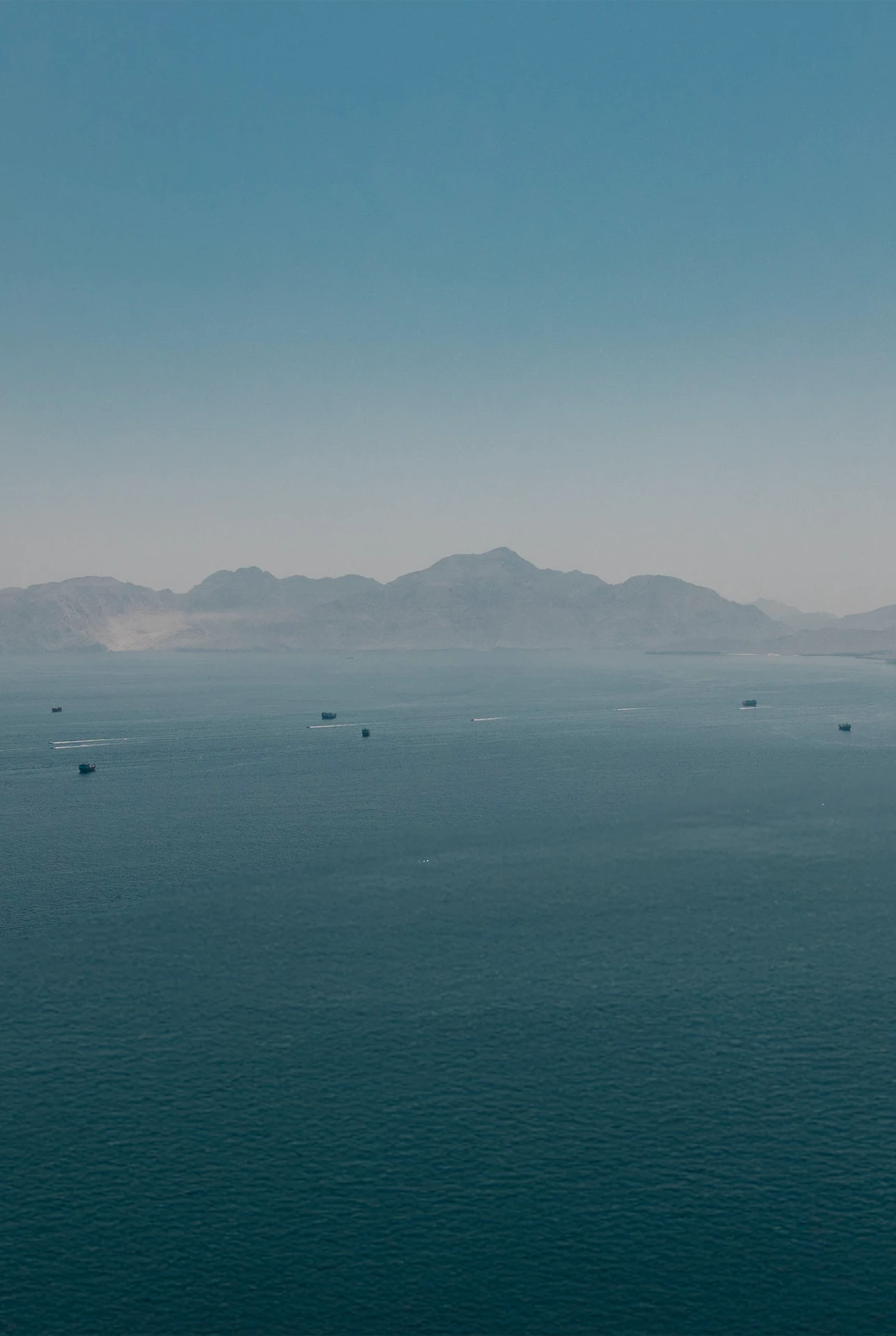 Ocean with mountains in the distance, with several fishing boats scattered across the horizon
