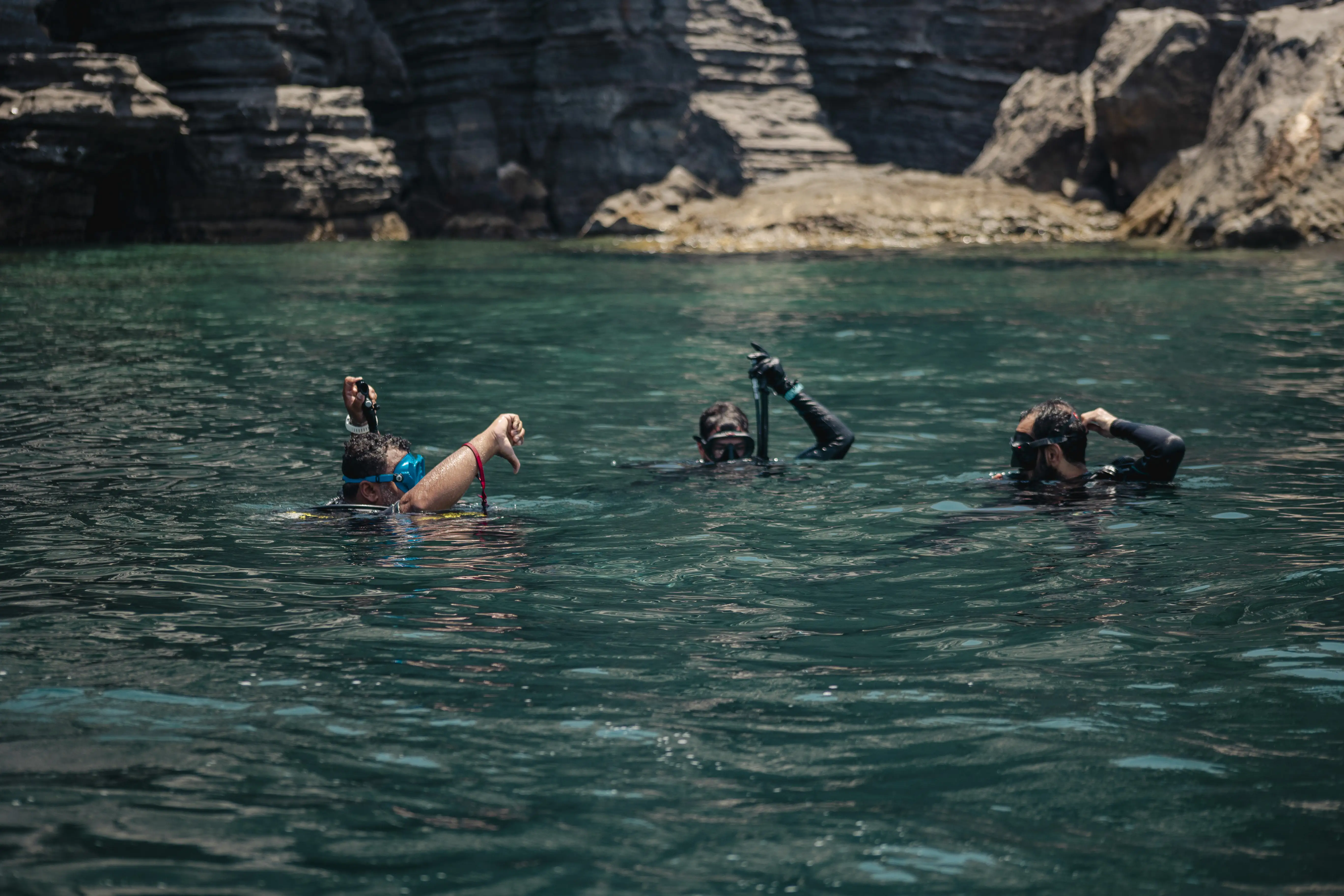 A group of scuba divers on the surface prepares to descend, with one giving the 'going down' hand signal.