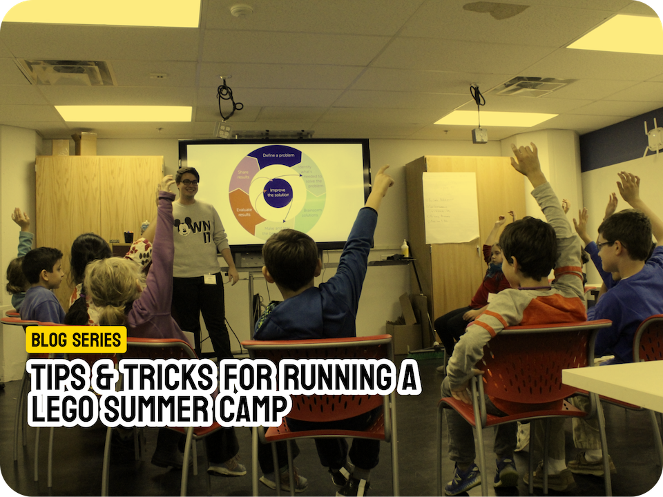 A classroom scene with children raising their hands toward an instructor, who stands in front of a presentation slide showing a problem-solving cycle. Overlaid text reads: "BLOG SERIES: TIPS & TRICKS FOR RUNNING A LEGO SUMMER CAMP."