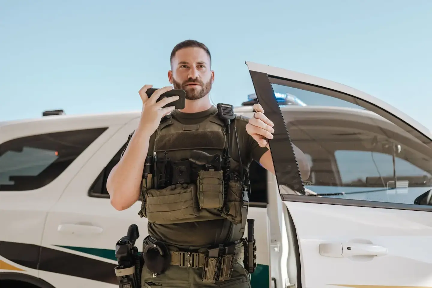 A police officer steps out of a patrol car while he talks on Tango Tango PTT on a smartphone