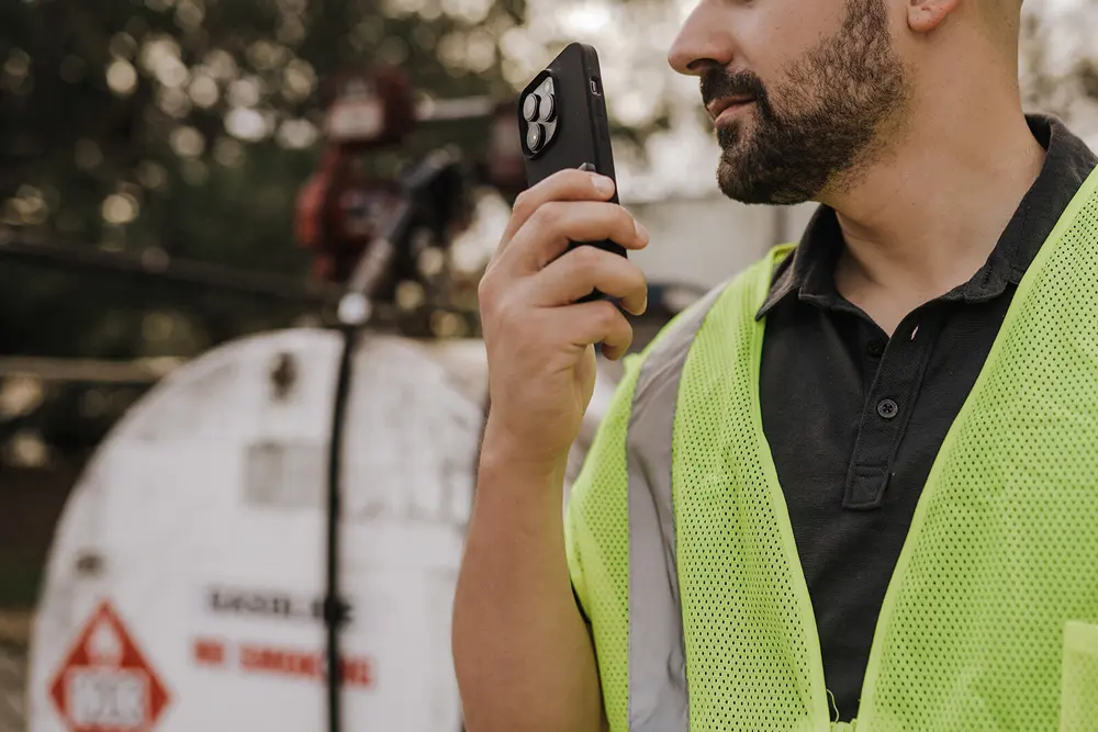 A construction worker uses Tango Tango PTT on his smartphone standing in front of a propane tank