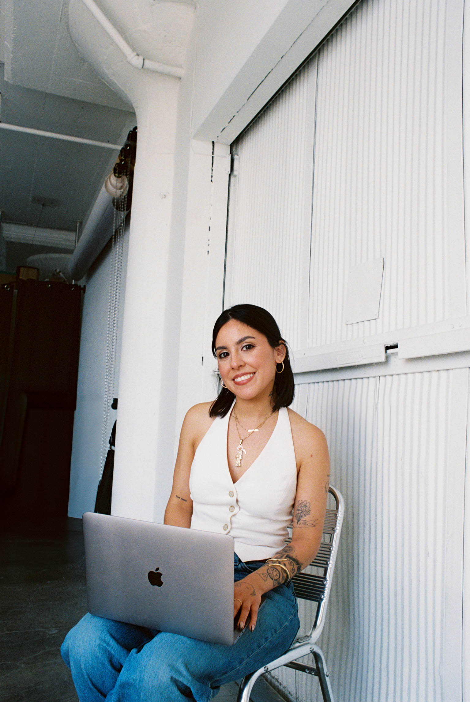Image of Mayra sitting on chair with laptop on lap