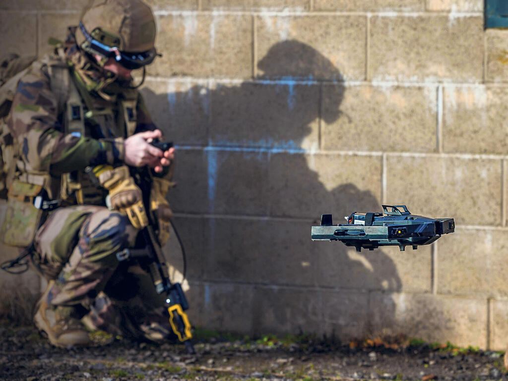 An operator kneeling against a wall, flying a SKYLORD GRIFFON drone hovering to his right