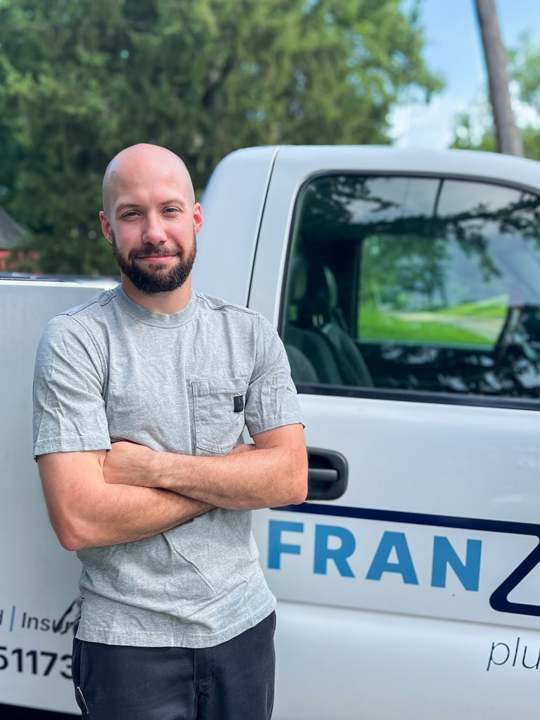 Franzen Plumbing owner Ben Franzen standing in front of truck with arms crossed