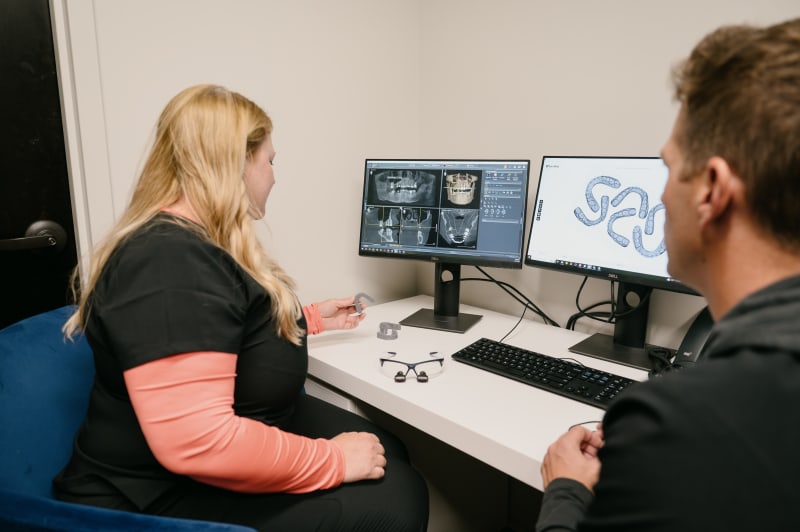 Female dentist consulting with male patient at desk in treatment room