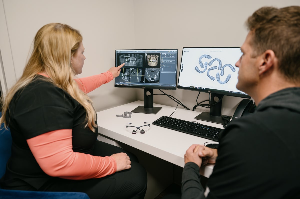 Dental professional reviewing X-ray images with patient on monitor screen