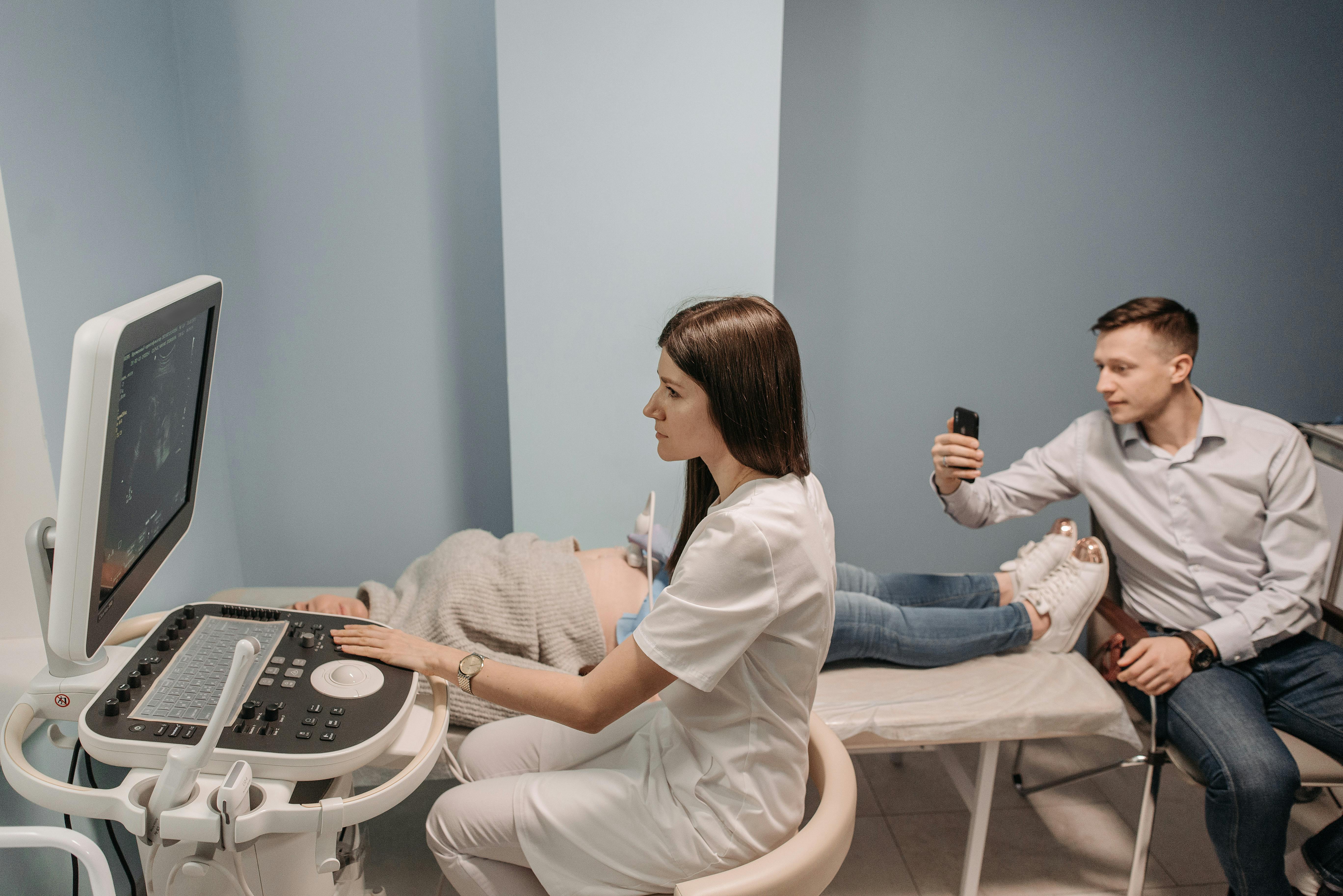 A man recording the ultrasound screen while a pregnant woman is getting an ultrasound. 
