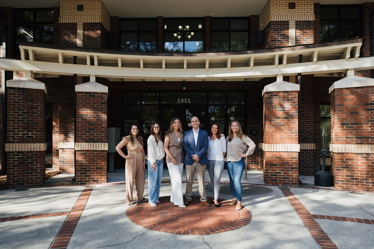 Group of five women and one man standing in front of a brick building entrance with the number 1951 above the door.