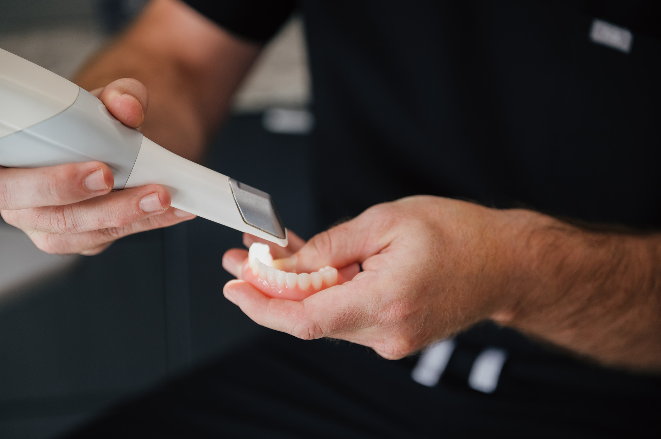 Person holding a dental scanner close to a set of artificial teeth in their hand.