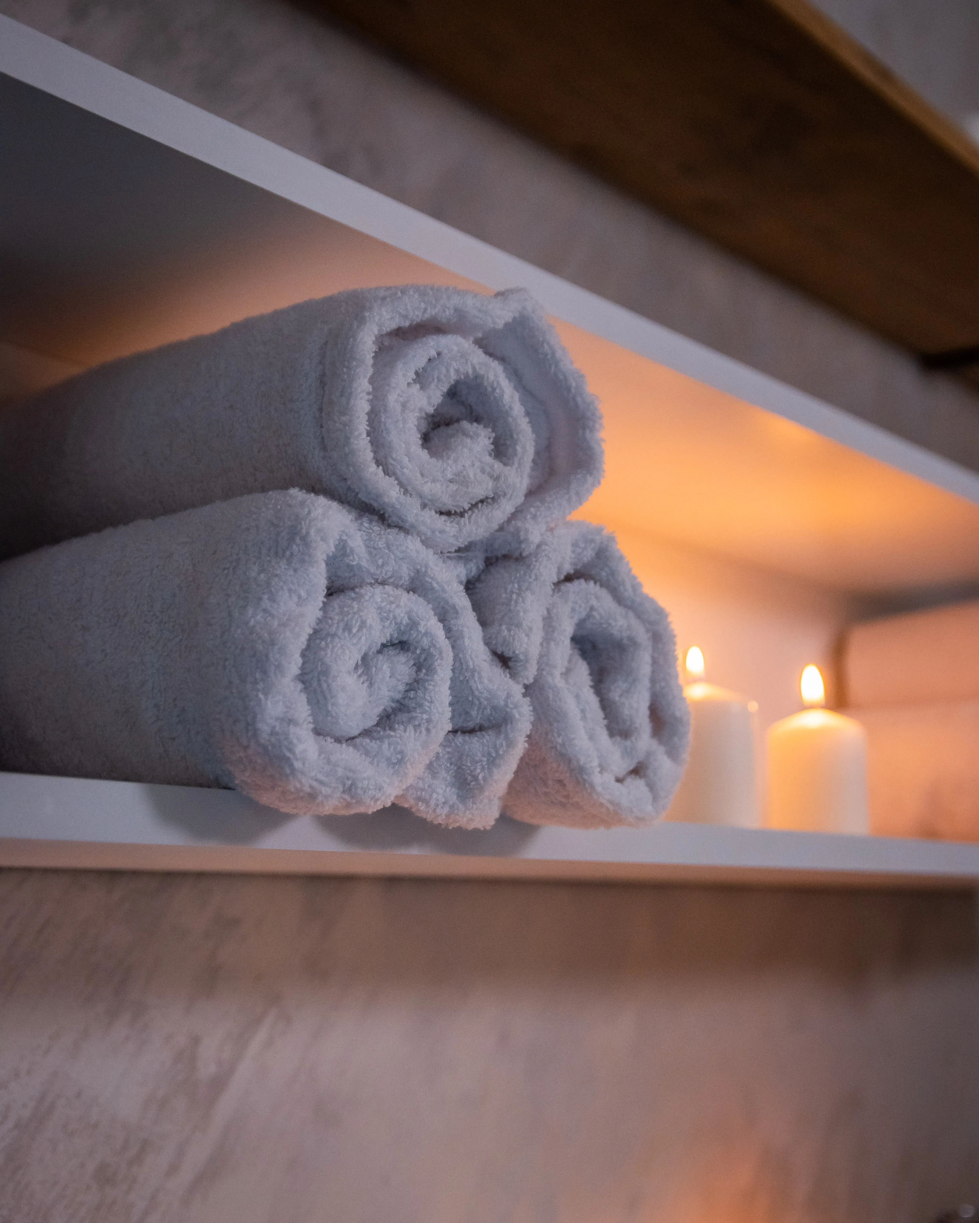 Urolani beli peškiri i sveće na polici sa toplim osvetljenjem u Runway Massage studiju.