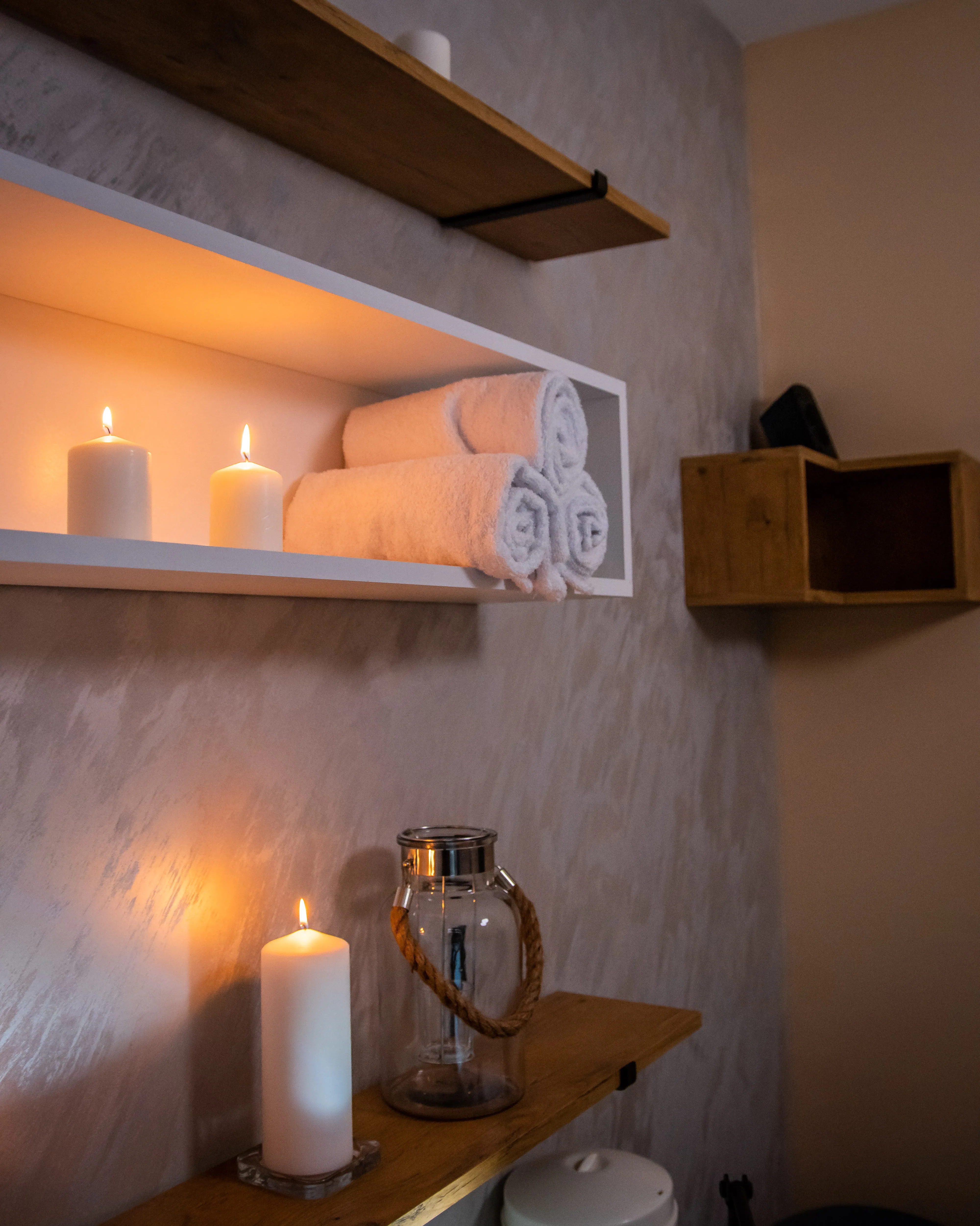 Zid sa više polica na kojima su urolani peškiri, upaljene sveće i dekorativni svecnjak u luksuznom ambijentu Runway Massage studija.