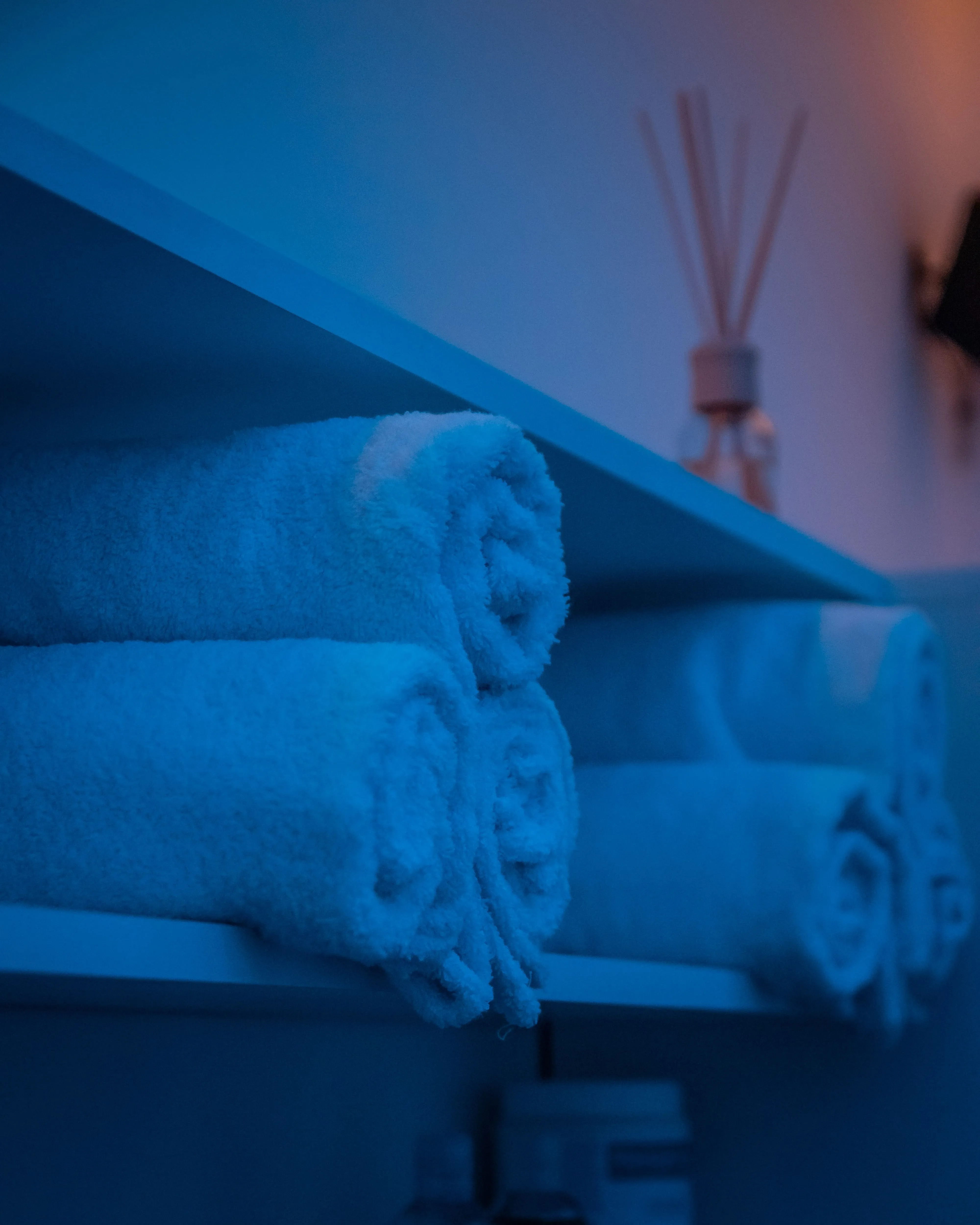 Dekorativno urolani peskiri na polici u sobi sa plavim svetlom u Runway Massage.