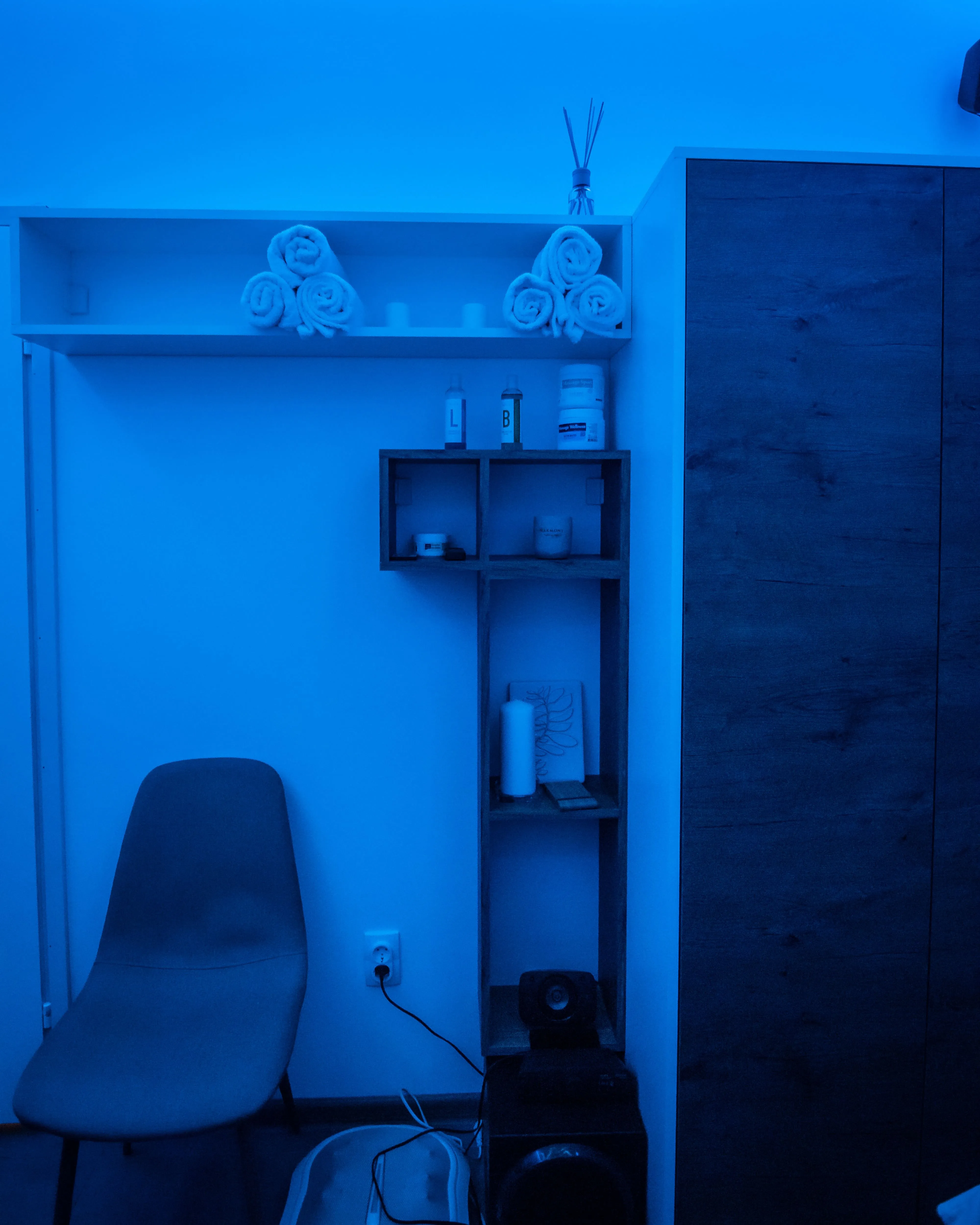 Stolica, police i ormar sa dekorativnim detaljima u sobi sa plavim svetlom u Runway Massage.
