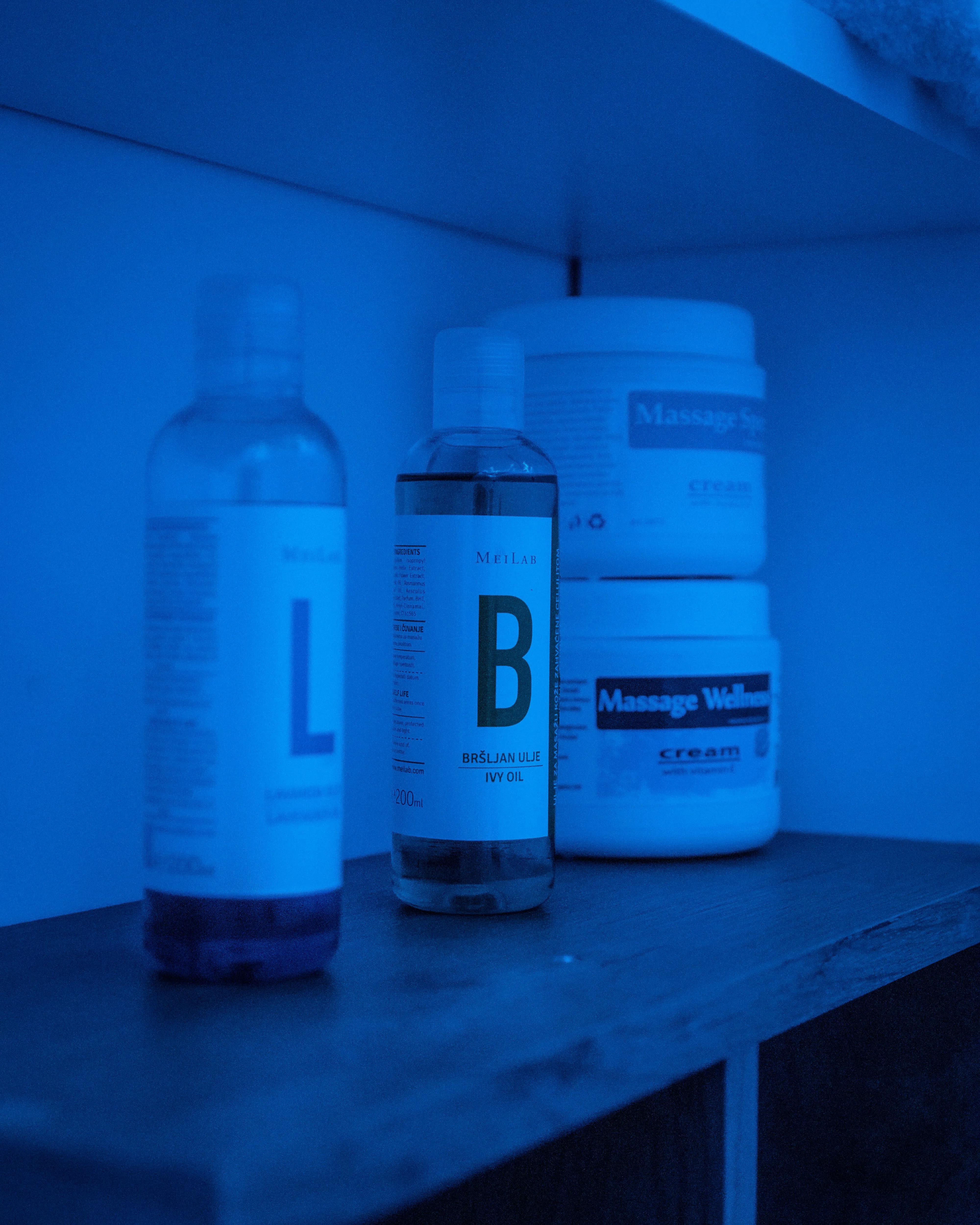 Flašice sa uljima i kreme za masažu na polici pod plavim ambijentalnim svetlom u Runway Massage studiju.