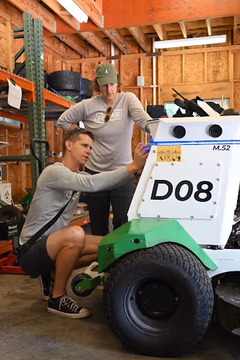 Two people examining a Scythe Mower Robot