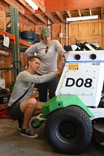 Two people examining a Scythe Mower Robot