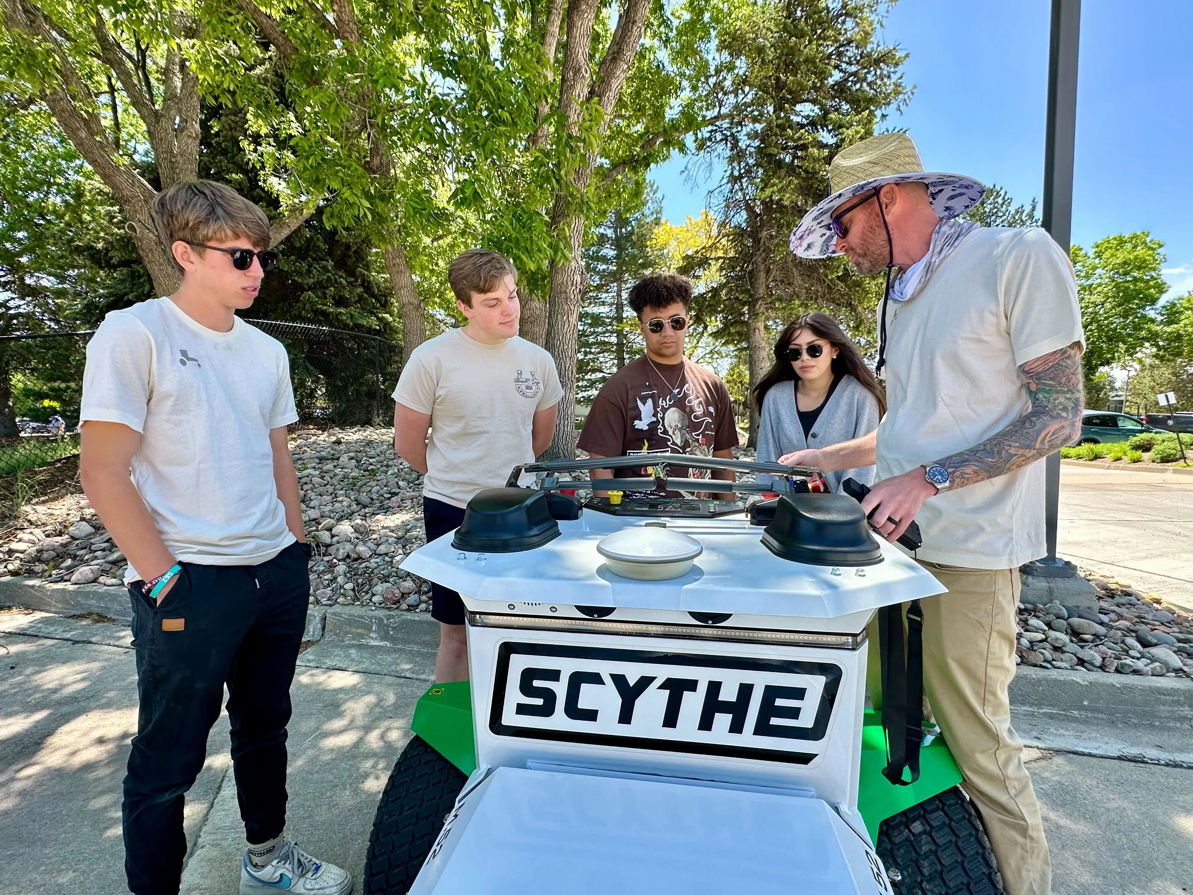Photo of five people huddled around a Scythe Mower Robot examining it
