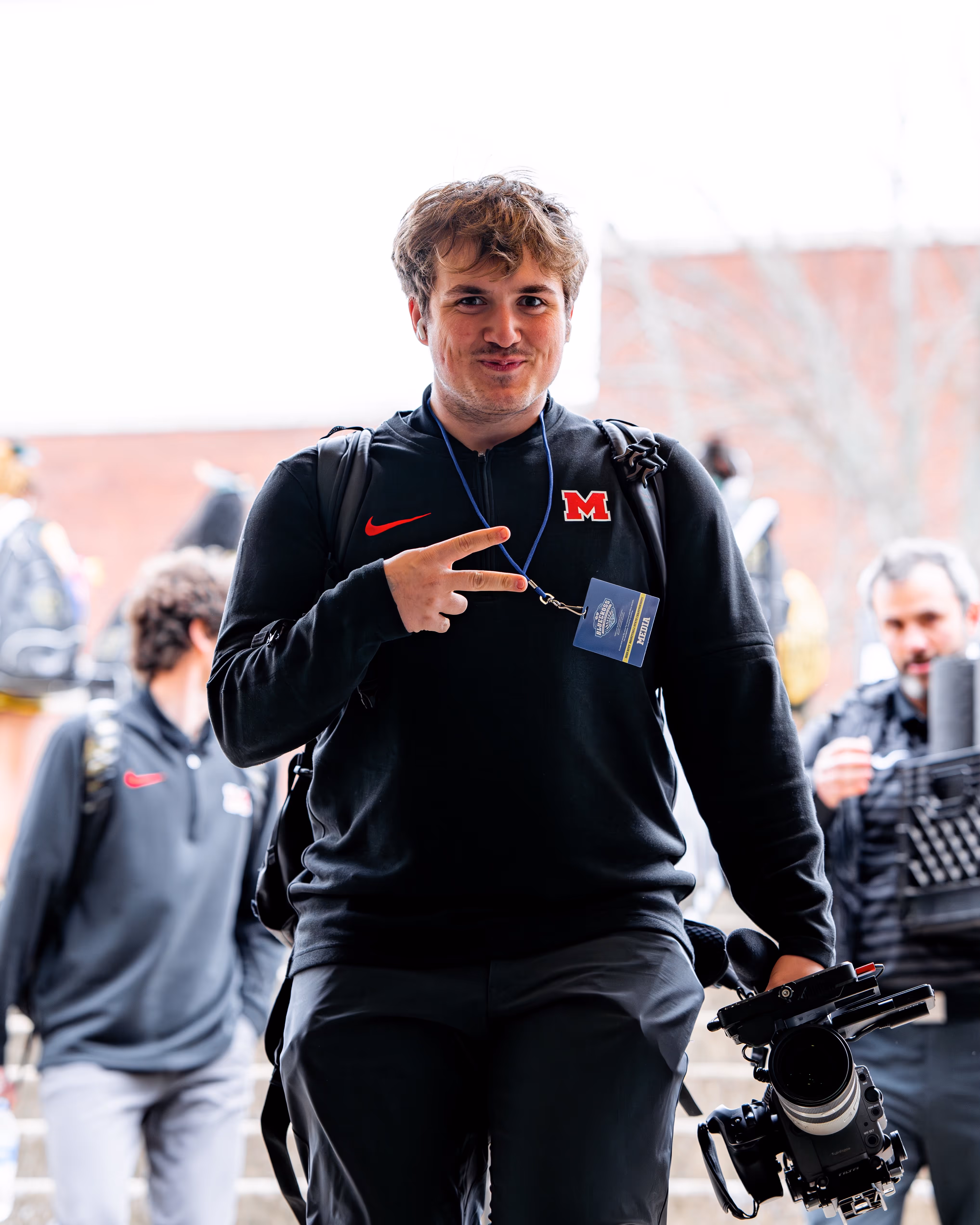 CJ Newton, founder of Newton Creative, walking with his camera in one hand and giving a peace sign with the other. 