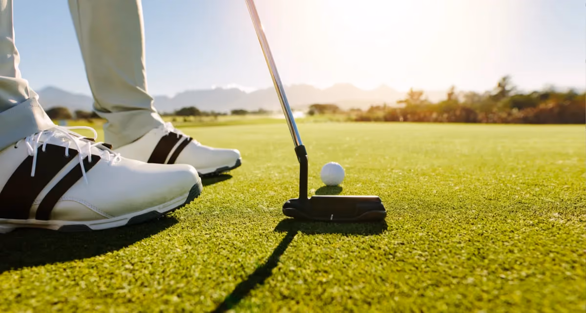 A closeup at ground level of a golfer's feet, club and ball
