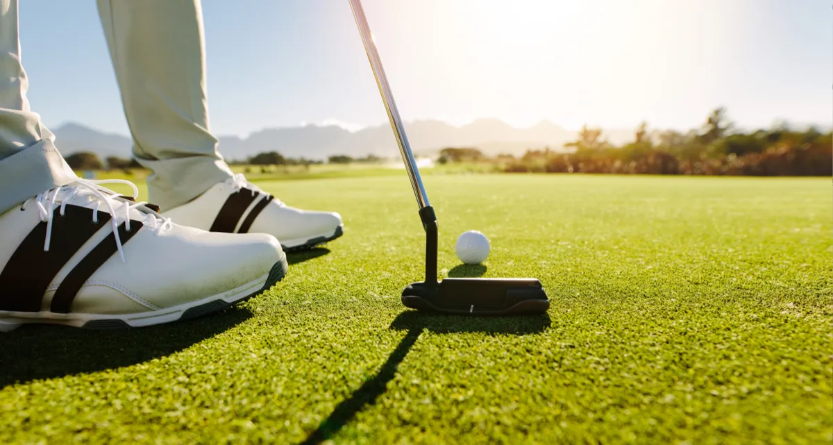A closeup at ground level of a golfer's feet, club and ball