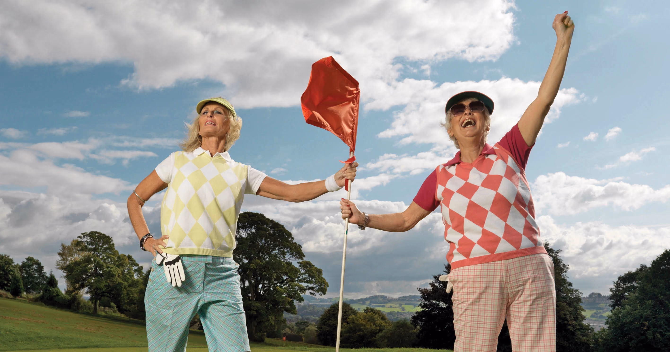 Two people in golf clothing holding onto a flag