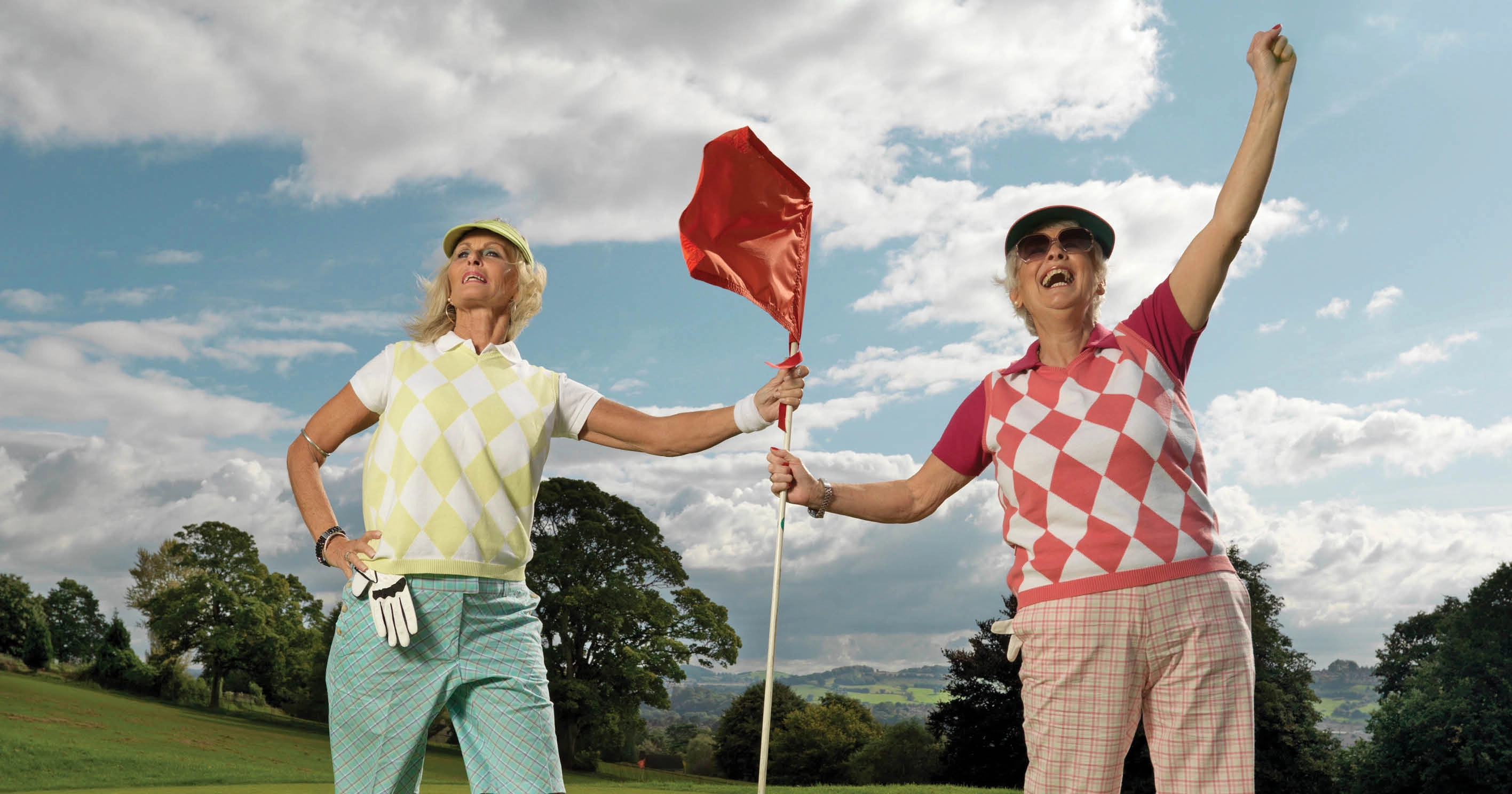 Two people in golf clothing holding onto a flag