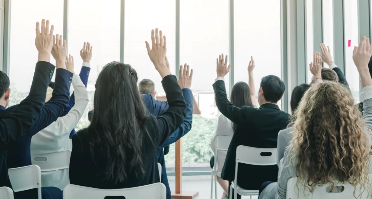 A group of people sitting on chairs raising their hands